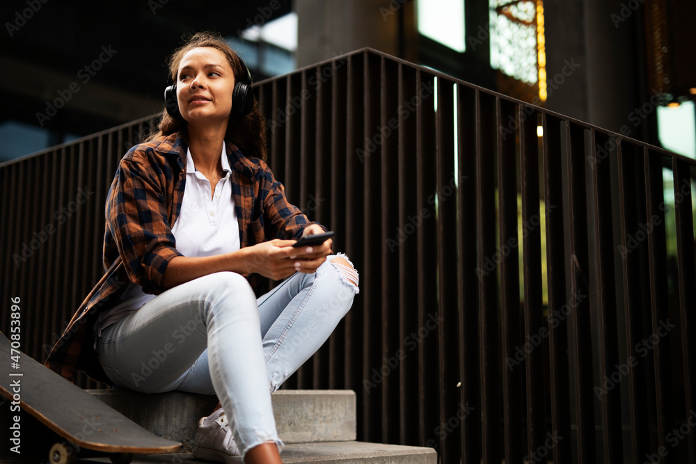Beautiful young girl with skateboard. Urban brunette woman listening the music outside. Beautiful young girl with skateboard. Urban brunette woman listening the music outside.