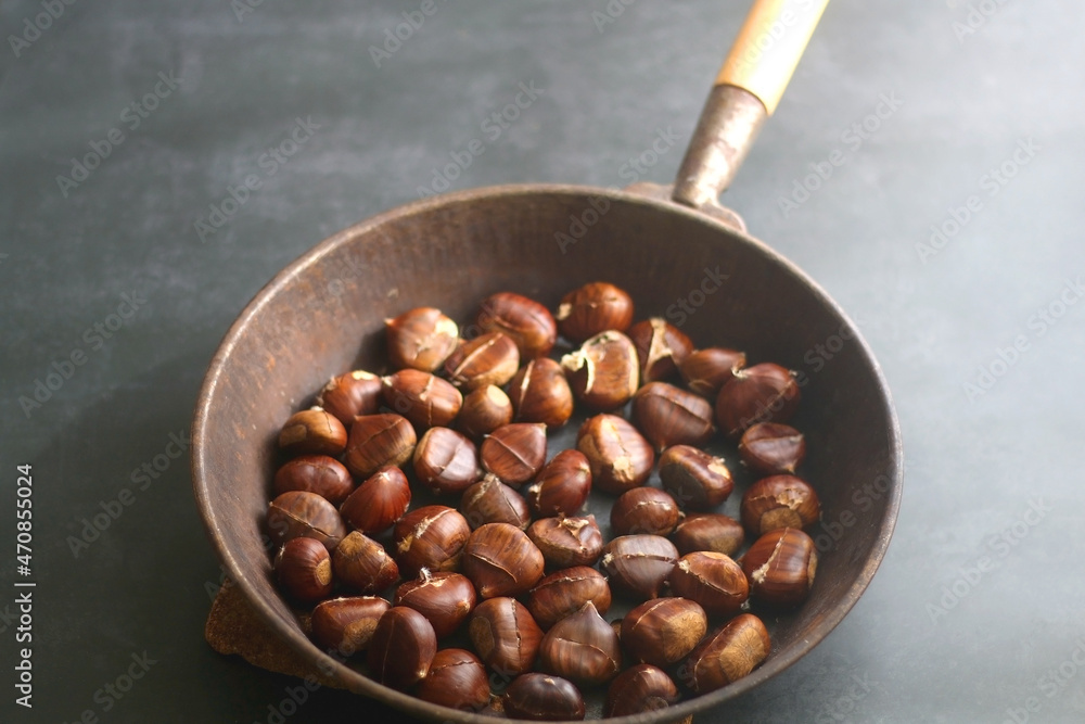 Fototapeta premium Pan filled with chestnuts on dark background. Selective focus.