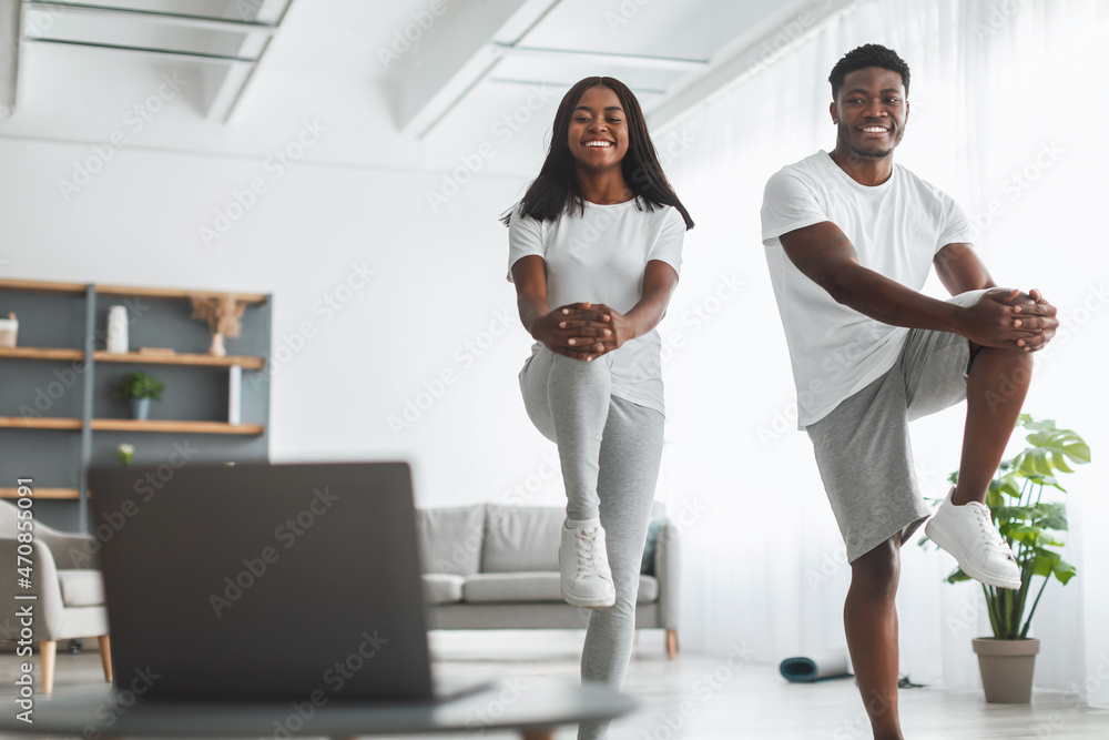 Obraz premium Young black couple doing high knee exercise with pc