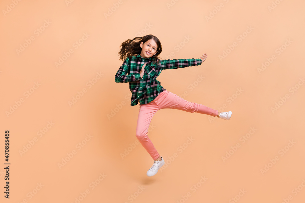Photo of funky strong school girl dressed checkered clothes jumping high practicing karate isolated beige color background Photo of funky strong school girl dressed checkered clothes jumping high practicing karate isolated beige color background