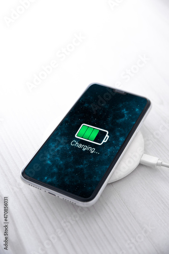 Mobile smart phone on wireless charging device on white background. Icon battery and charging progress lighting on screen.smartphones connected to power source.low battery level problems.Plugged Phone