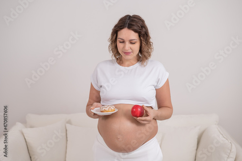 A pregnant woman is holding a red apple and donut. Choice of food. photo