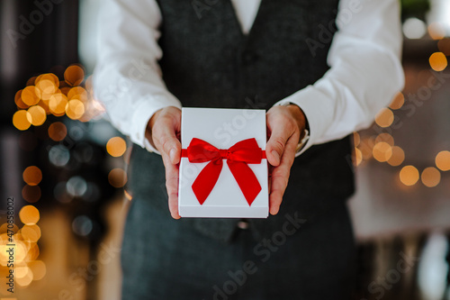 Business man holding white present box with red ribbon in the room