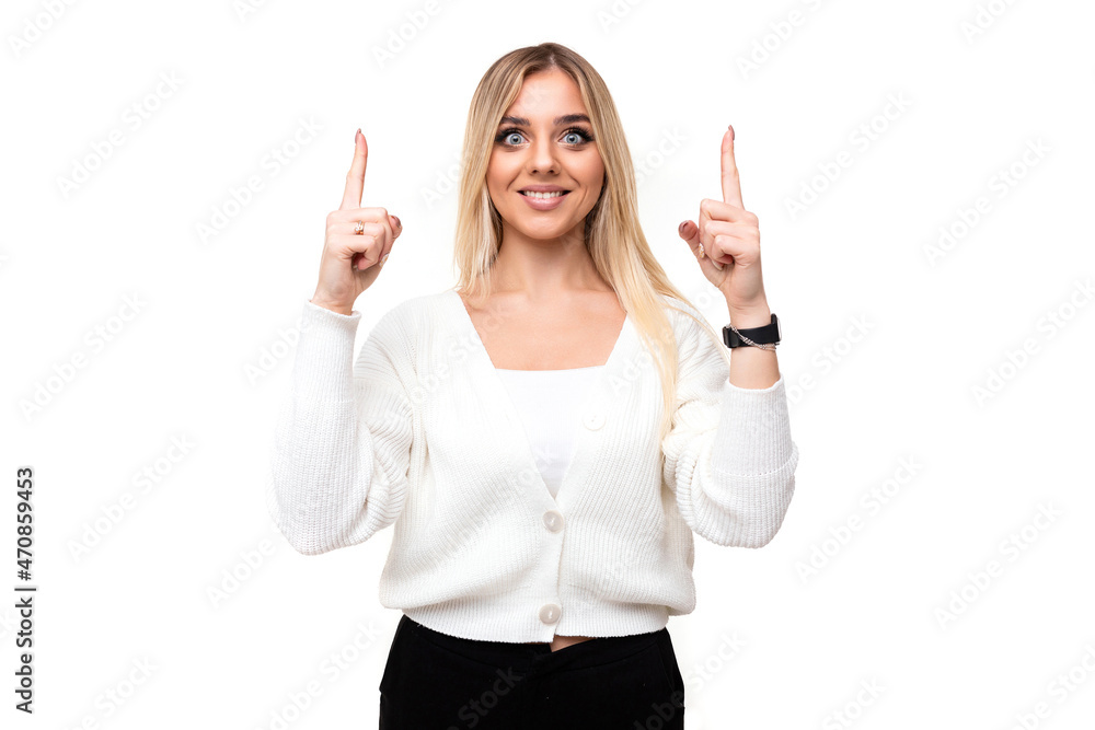 Photo of a beautiful positive happy smiling young blonde woman with makeup in a stylish white knitted sweater and black pants shows fingers up isolated on a white background with empty space for text Photo of a beautiful positive happy smiling young blonde woman with makeup in a stylish white knitted sweater and black pants shows fingers up isolated on a white background with empty space for text