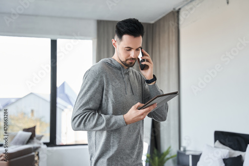 Man chatting via smartphone while looking at the tablet screen at home