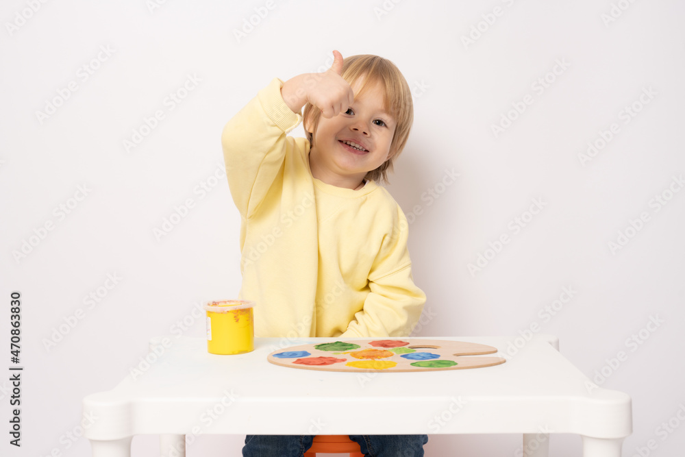 Inspired little boy at the table drawing with thumb up isolated on white Inspired little boy at the table drawing with thumb up isolated on white