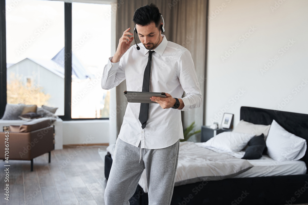 Man wearing headset looking at the tablet while working with clients from home Man wearing headset looking at the tablet while working with clients from home