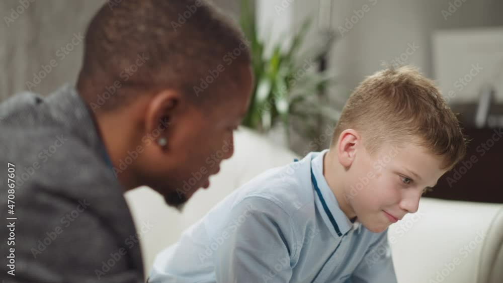 Young black man tutor conducts private English lesson to primary schoolboy at homeschooling with native speaker in living room closeup slow motion Young black man tutor conducts private English lesson to primary schoolboy at homeschooling with native speaker in living room closeup slow motion