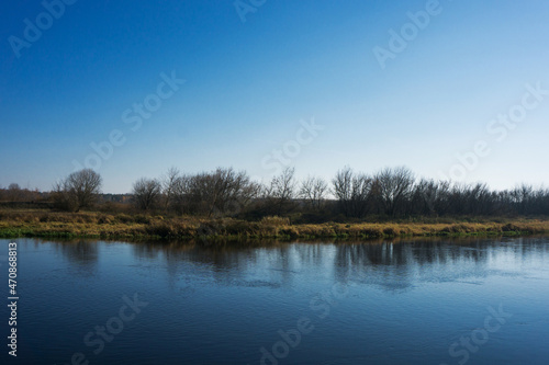 Winter river shore background. Autumn lake shore landscape. Blue sky and tranquil water flow.