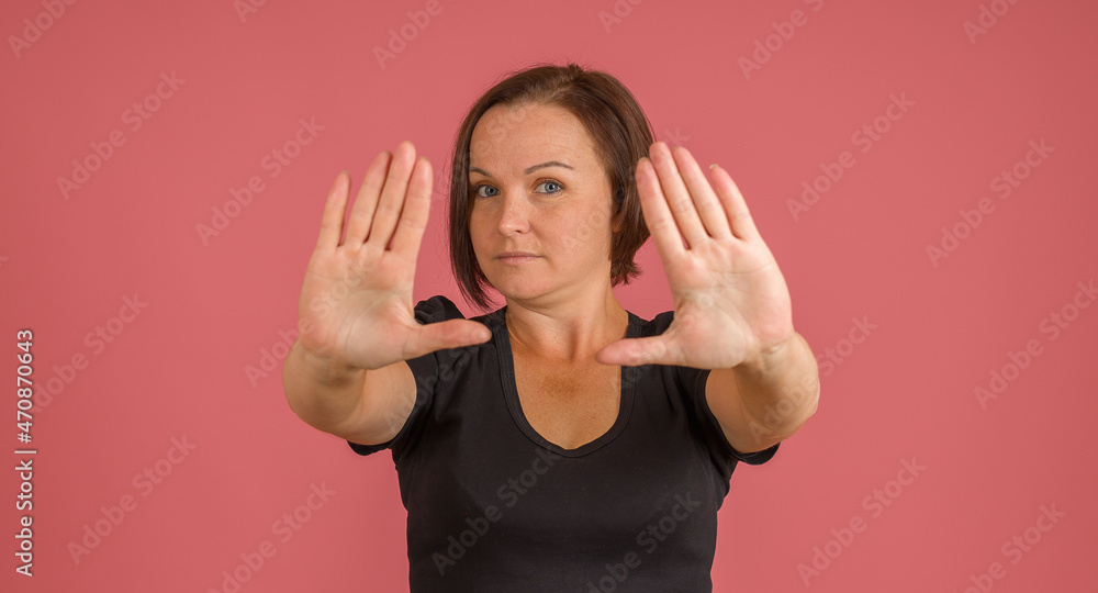 woman in black t-shirt put out her palms in front, stop sign, pink background woman in black t-shirt put out her palms in front, stop sign, pink background