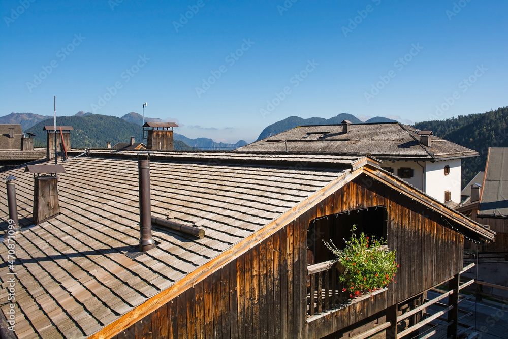 Rooftops of traditional wooden buildings in the Alpine village of Sauris di Sopra, Udine Province, Friuli-Venezia Giulia, north east Italy. The foreground roof has a snow guard trunk and tall chimneys