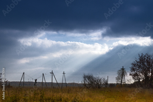an old electrical substation in a field lit by the rays of the sun breaking through the blue clouds
