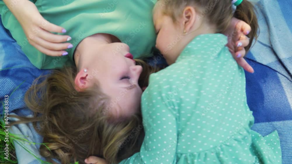 Mom and daughter are laughing while lying on the blanket. Top view. Emotions of mom and daughter. Mom and daughter are laughing while lying on the blanket. Top view. Emotions of mom and daughter.