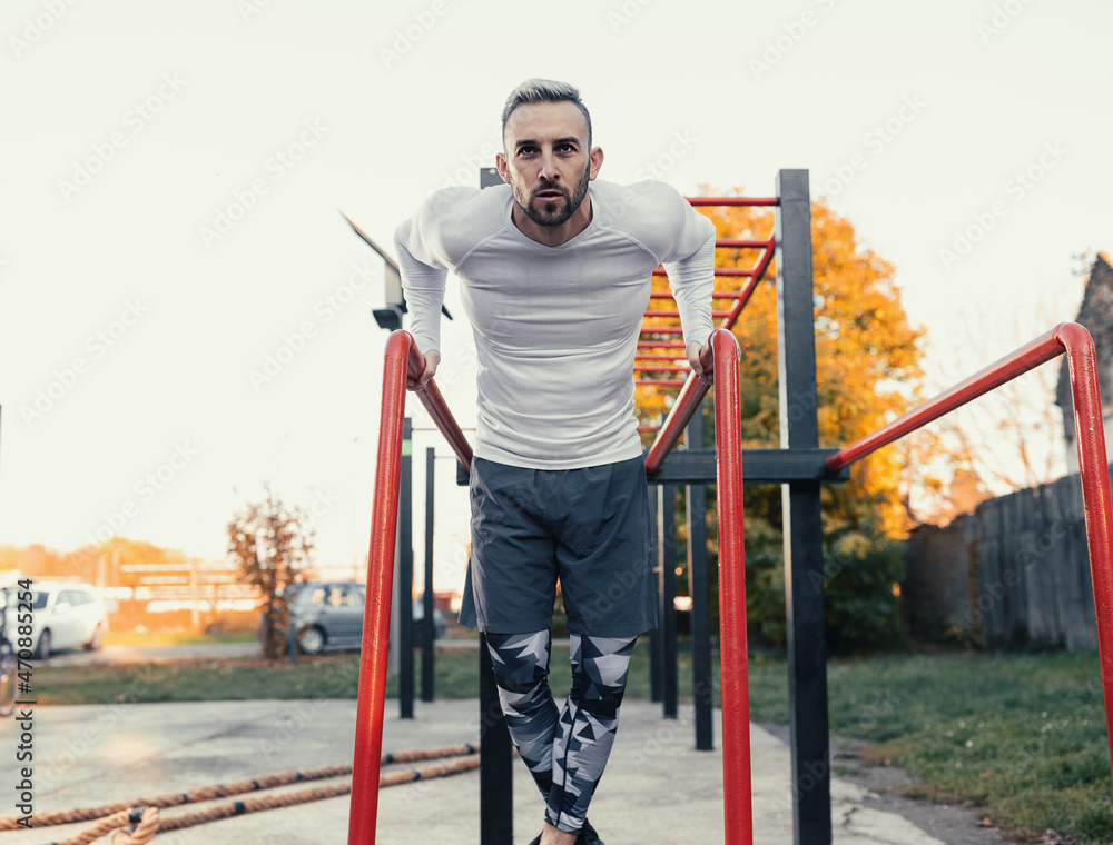 Muscular good looking man doing dips on parallel bars, chest workout outdoors