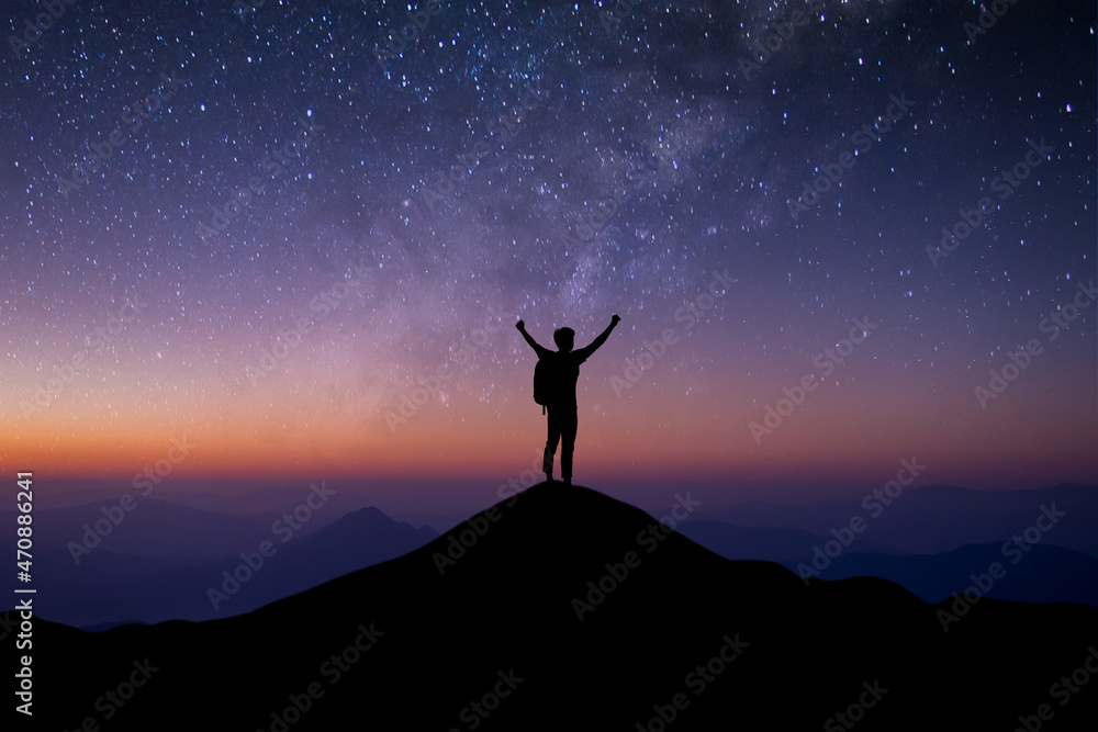 Young traveler with backpack standing and open both arm and watched night sky view, star and milky way alone on top of the mountain. He enjoyed traveling and was successful when he reached the summit.