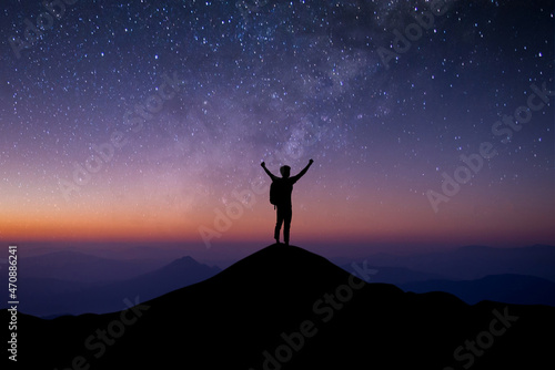 Young traveler with backpack standing and open both arm and watched night sky view, star and milky way alone on top of the mountain. He enjoyed traveling and was successful when he reached the summit.