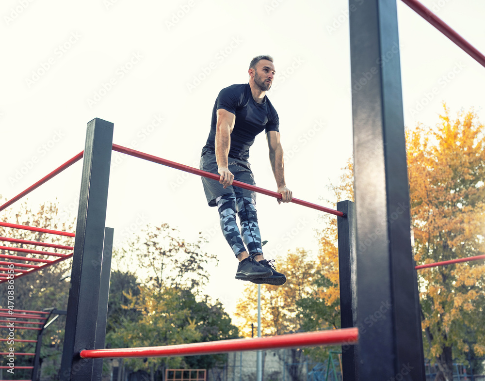 Muscular young man working out on the bar outside, street workout