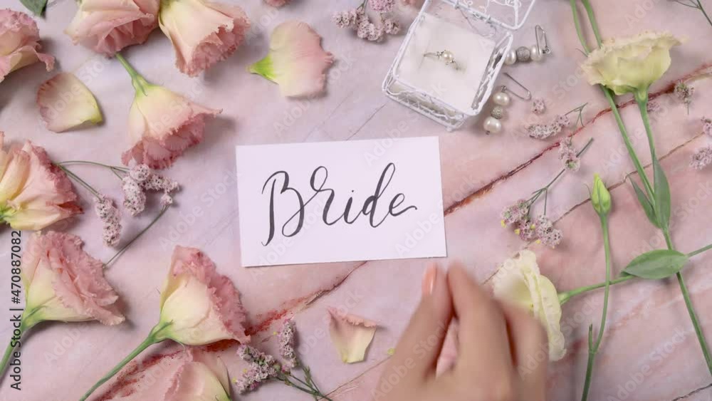 Hand puts BRIDE card on a marble table near pink flowers close up Hand puts BRIDE card on a marble table near pink flowers close up