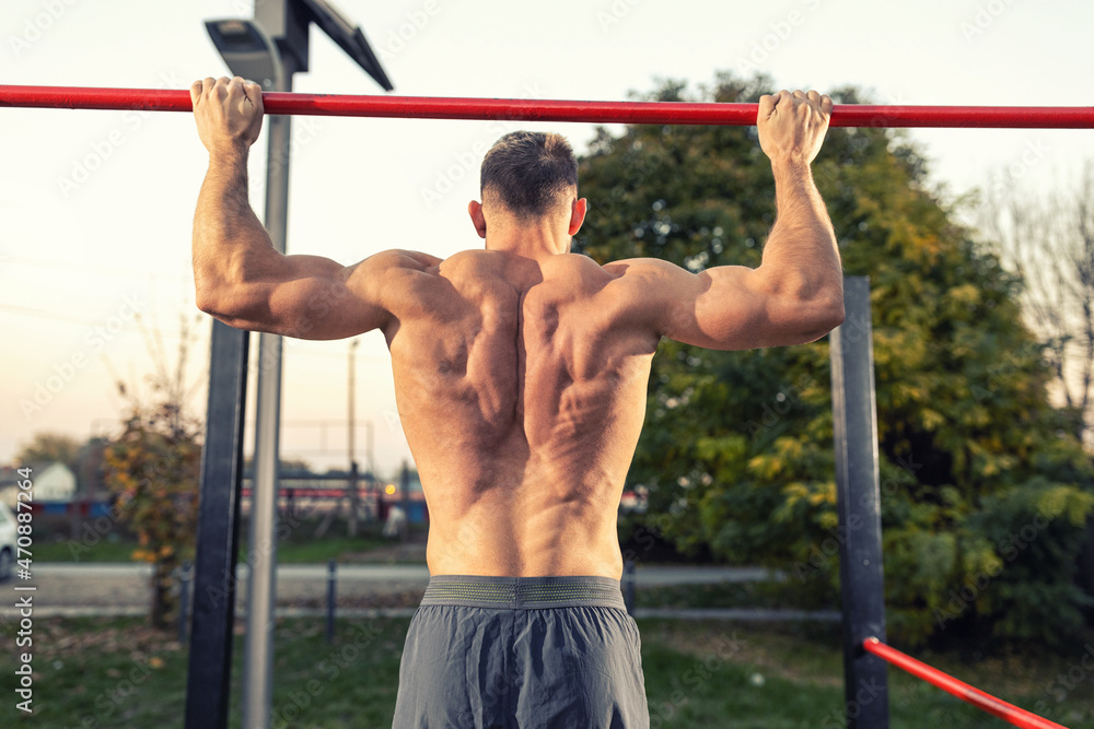 Shirtless ripped young man doing pull ups outdoors and showing definition on his back muscles