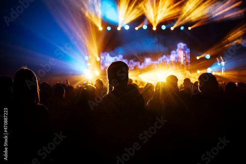 silhouette of the audience at a music concert. the happy audience dances and applauds their idols. bright multicolored spotlights illuminate the stage and the auditorium