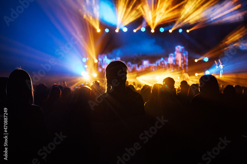 silhouette of the audience at a music concert. the happy audience dances and applauds their idols. bright multicolored spotlights illuminate the stage and the auditorium