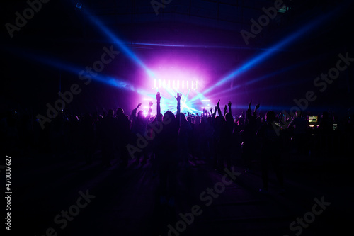 happy fans of a musical group dance at a concert. the bright light of the spotlights shines on thousands of spectators