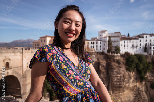 Glad Asian woman sitting near historic bridge in Ronda photo