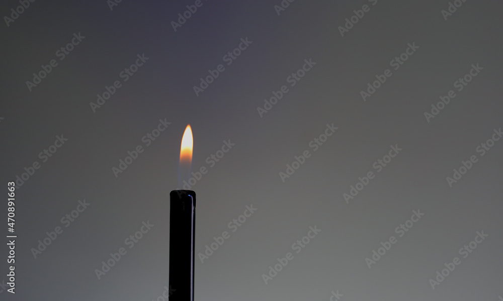 Metallic black barrel of lighter fueled with liquid gas with bright hot burning orange yellow even flame on solid gray background closeup Metallic black barrel of lighter fueled with liquid gas with bright hot burning orange yellow even flame on solid gray background closeup