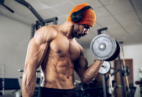 Muscular shirtless ethnic bodybuilder in headphones lifting dumbbell photo