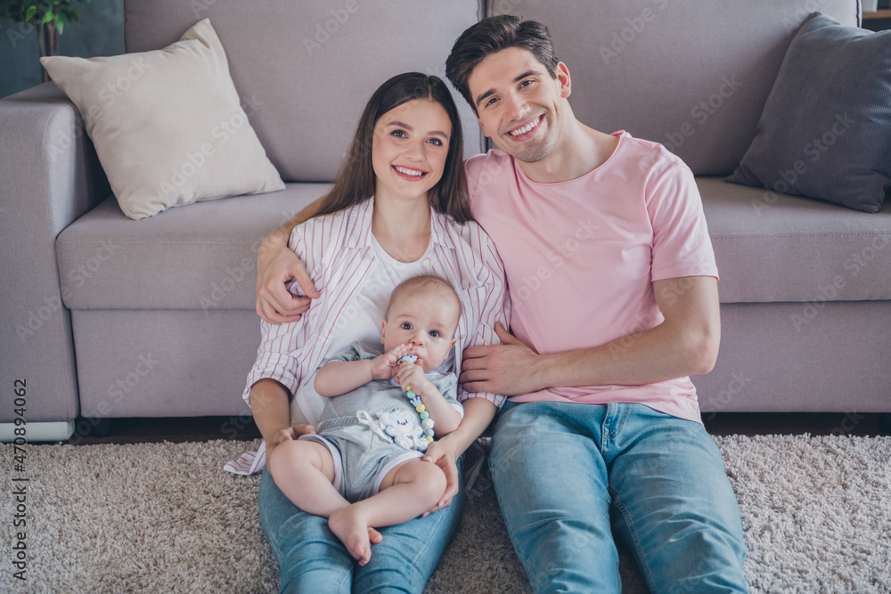 Portrait of attractive sweet tender cheerful full family holding baby sitting on carpet cuddling pastime at home indoors Portrait of attractive sweet tender cheerful full family holding baby sitting on carpet cuddling pastime at home indoors