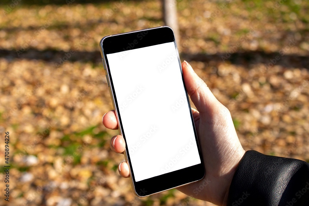 Woman holding smartphone with blank white screen on nature background.