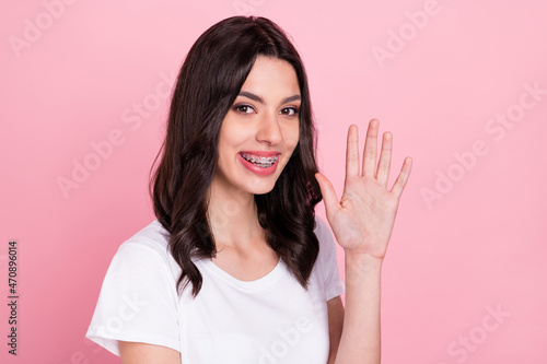 Photo of cheerful young happy positive woman wave hand hello good mood isolated on pastel pink color background