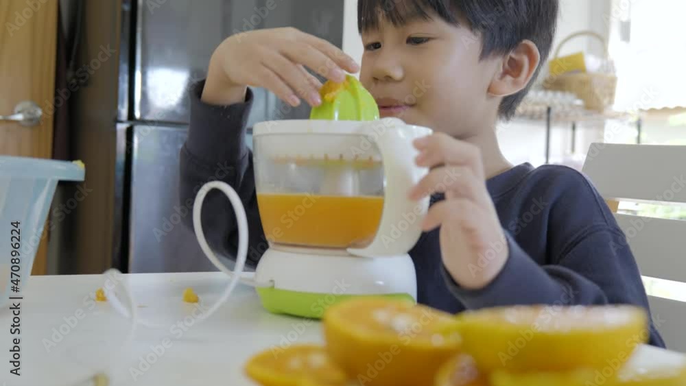 Asian boy making fresh orange juice by automatic juicer for the breakfast. Asian boy making fresh orange juice by automatic juicer for the breakfast.