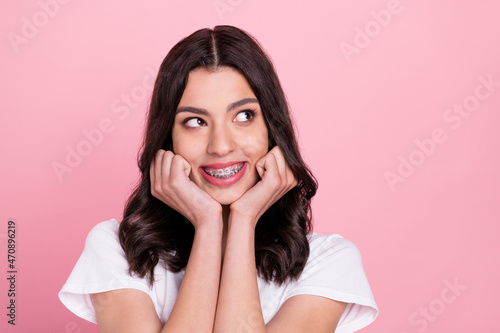 Photo of adorable happy young woman look empty space wear teeth braces isolated on pink color background photo