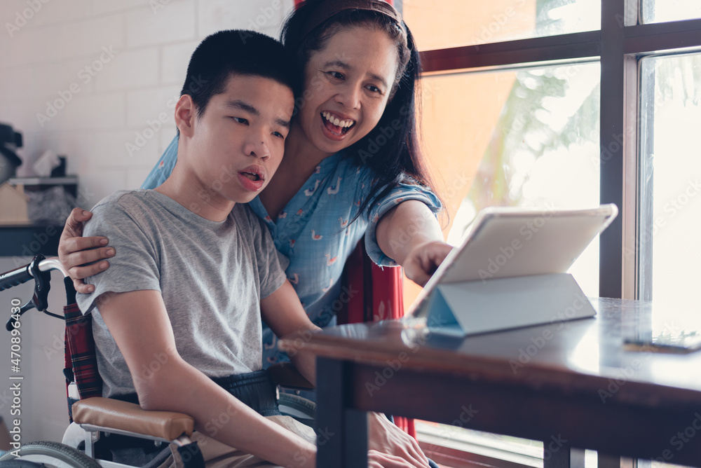 Young man with a disability and mother using tablet computer in home for education remote or video chat or shopping online in warm cinema tone, Social media and people use technology concept. Young man with a disability and mother using tablet computer in home for education remote or video chat or shopping online in warm cinema tone, Social media and people use technology concept.
