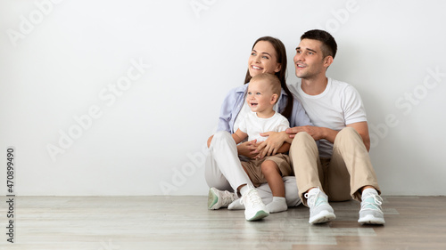 Beautiful Young Family With Little Baby Looking Aside While Relaxing On Floor © Prostock-studio
