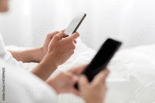 Unrecognizable european millennial guy and lady typing on smartphones with empty screen sits in bed, close up