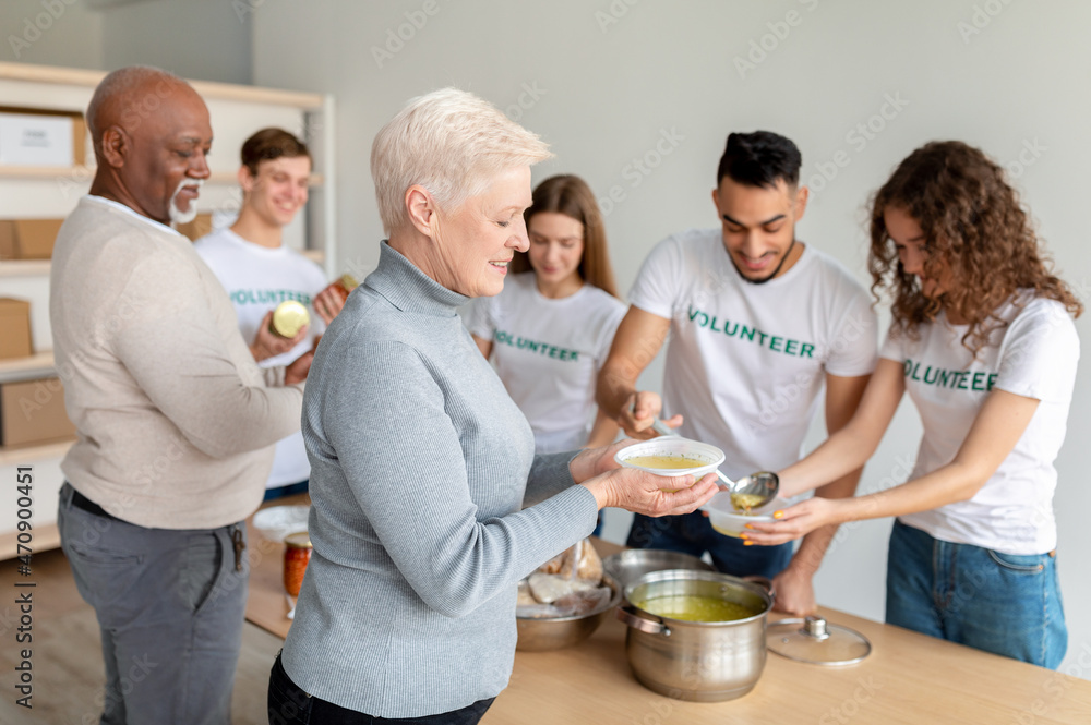 Happy senior woman received warm soup in charity organization office. Volunteer group helping feed elderly people Happy senior woman received warm soup in charity organization office. Volunteer group helping feed elderly people