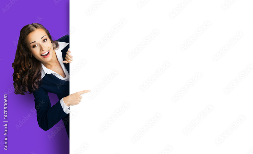 Happy excited woman in black suit showing pointing blank white mock up banner signboard. Business and advertising concept. Copy space empty place for text. Violet purple color background.. Happy excited woman in black suit showing pointing blank white mock up banner signboard. Business and advertising concept. Copy space empty place for text. Violet purple color background..