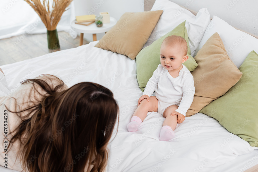 High angle view of young mother lying near baby daughter on bed. High angle view of young mother lying near baby daughter on bed.