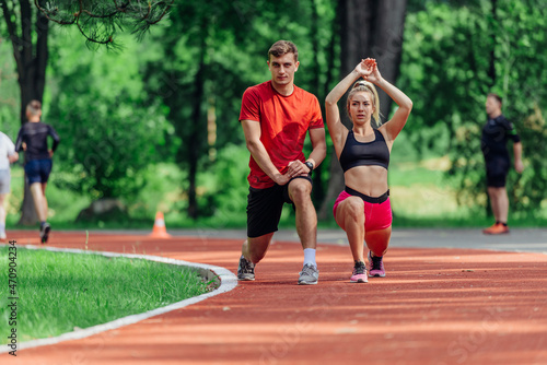 Young couple stretching before starting their morning jogging routine on a tartan track at the park. © qunica.com