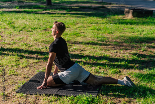Fotografie Healthy young man doing outdoors warmup stretching exercises on a fitness mat