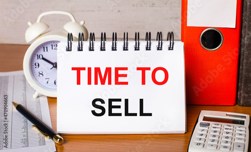 On the table are reports, a white alarm clock, a calculator, folders for papers, a pen and a white notebook with the TIME TO SELL. Business concept