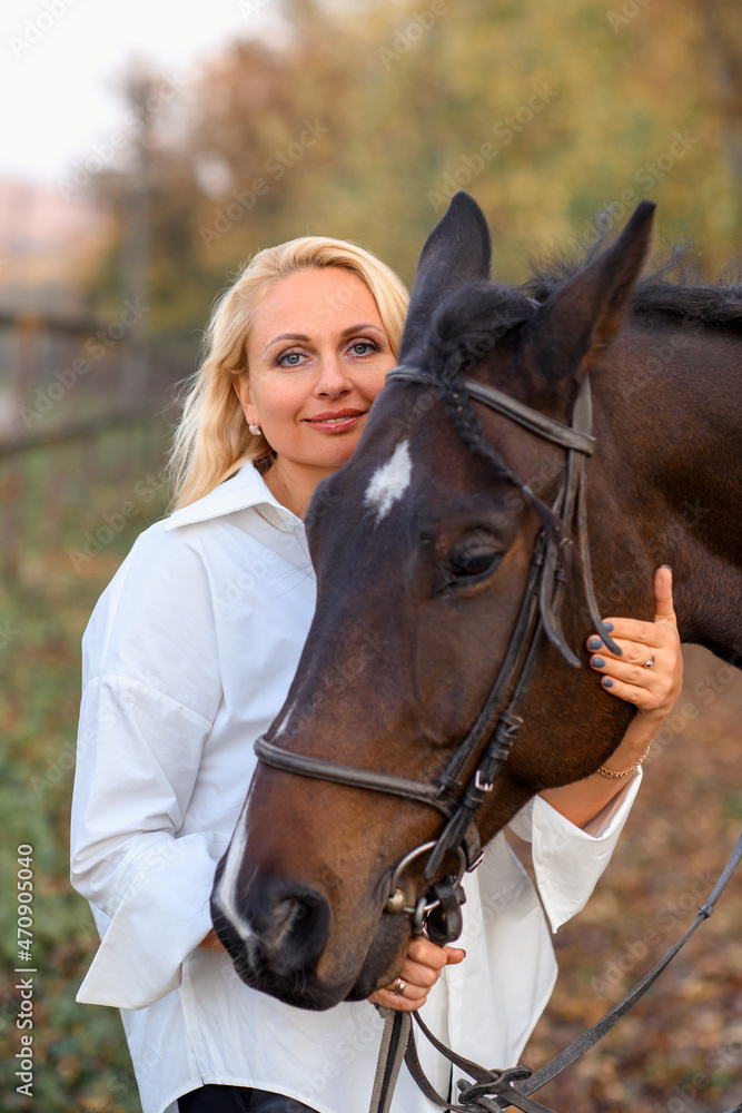 Obraz premium beautiful caucasian girl in a white shirt with a horse in the forest at sunset