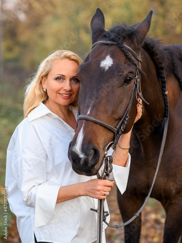 beautiful caucasian girl in a white shirt with a horse in the forest at sunset