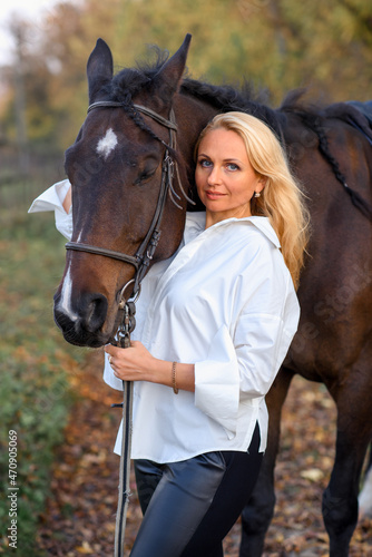 beautiful caucasian girl in a white shirt with a horse in the forest at sunset