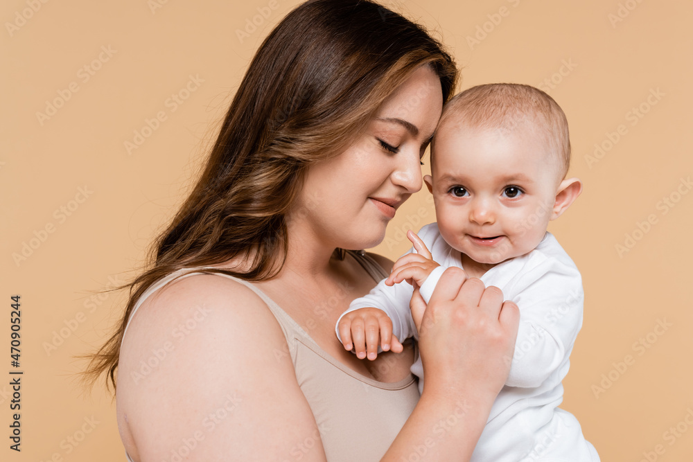 Brunette woman with closed eyes holding baby isolated on beige. Brunette woman with closed eyes holding baby isolated on beige.