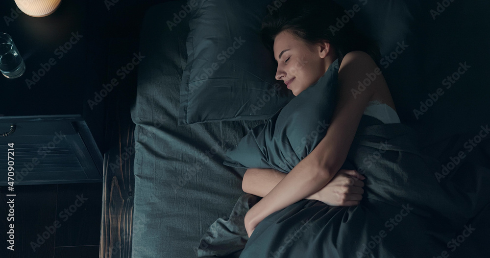 Beautiful young brunette woman sleeping on side, lying cozily in bed, hugging a pillow. Lady sound asleep at night. Loft interior. Beautiful young brunette woman sleeping on side, lying cozily in bed, hugging a pillow. Lady sound asleep at night. Loft interior.