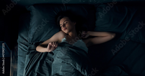 Brunette woman lying sound asleep in bed, changing position. A young caucasian lady is about to awake, stretching her arms while sleeping.