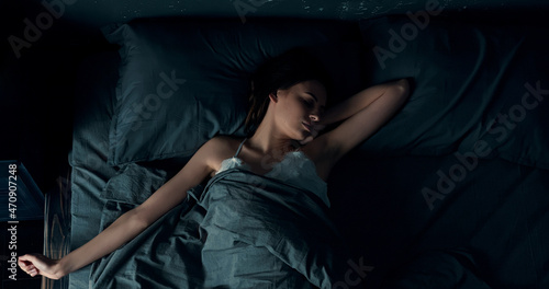Brunette woman lying sound asleep in bed, changing position. A young caucasian lady is about to awake, stretching her arms while sleeping.
